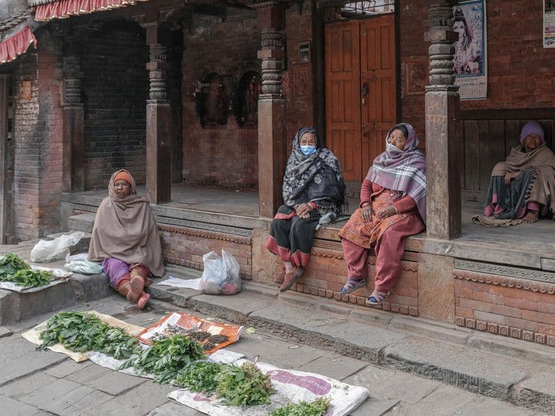 Four women in traditional clothing at a street market in Bhaktapur, Nepal, selling fresh produce.