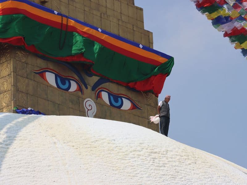 Boudhanath Stupa in Kathmandu with colorful prayer flags and a person walking on its dome.
