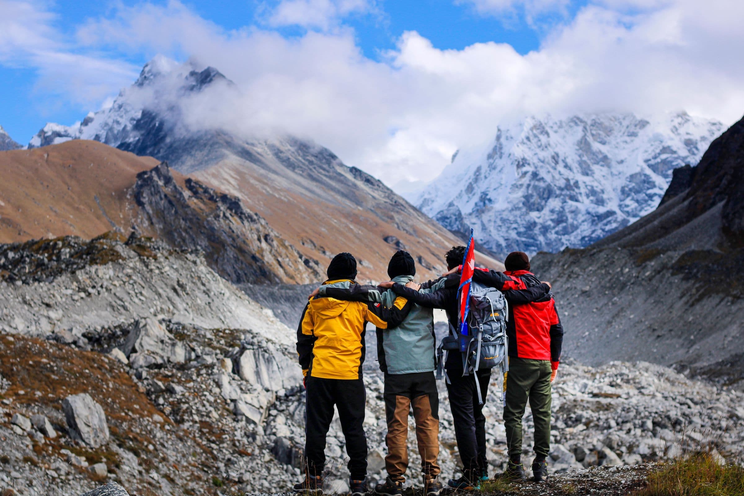 Four hikers stand arm in arm, embracing the majestic snowcapped mountain landscape.