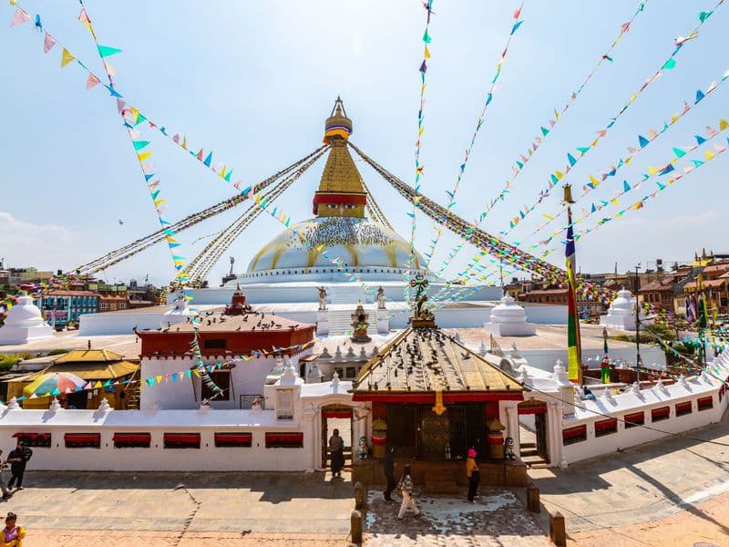 Vibrant scene of Boudhanath Stupa in Kathmandu, Nepal, adorned with colorful prayer flags and bustling with tourists.