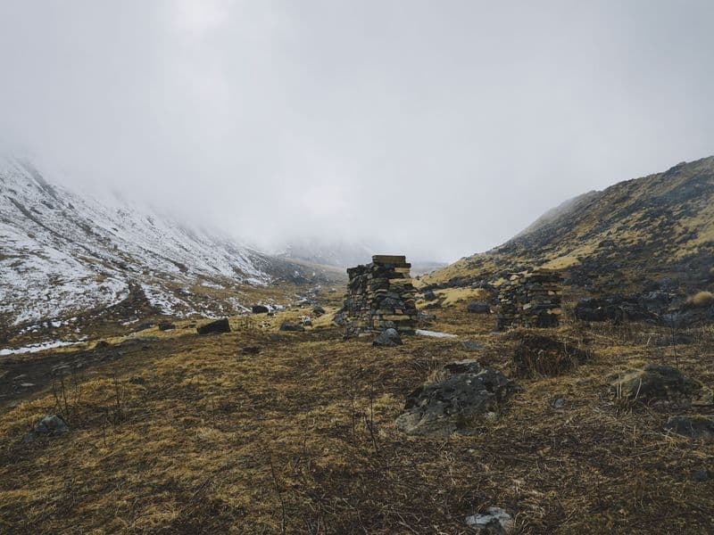 Explore the serene, snow-dusted mountains of Ghandruk, Nepal, featuring piled stones and misty skies.