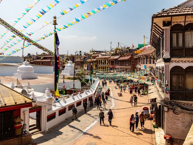 Colorful flags and lively streets around Boudhanath Stupa in Kathmandu, Nepal, with bustling activity.