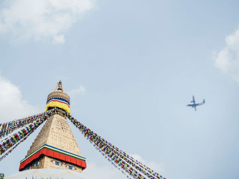 Boudhanath Stupa in Kathmandu, Nepal with vibrant prayer flags and an airplane in the sky.