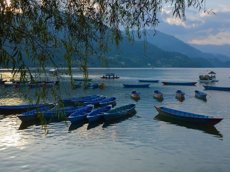 Peaceful scene of blue rowboats on a calm lake at sunset with mountain backdrop.