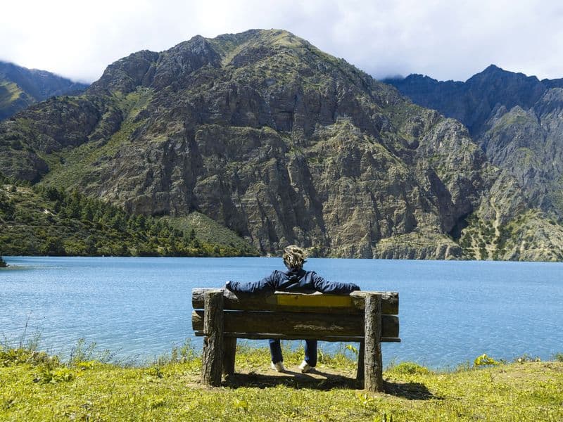 A person relaxes on a bench by Phoksundo Lake in Nepal amidst stunning mountain scenery.